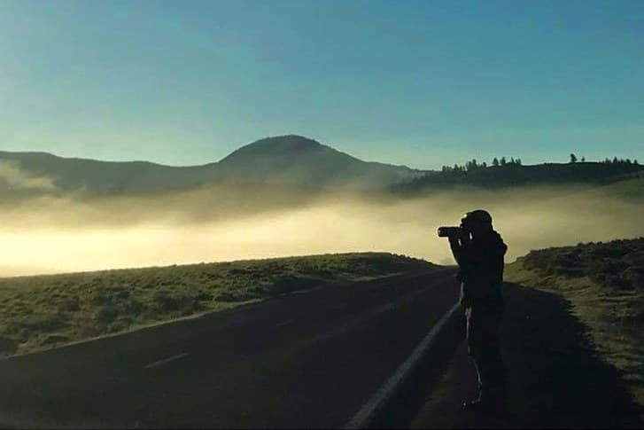 Photographer shooting a foggy sunrise over rolling hills
